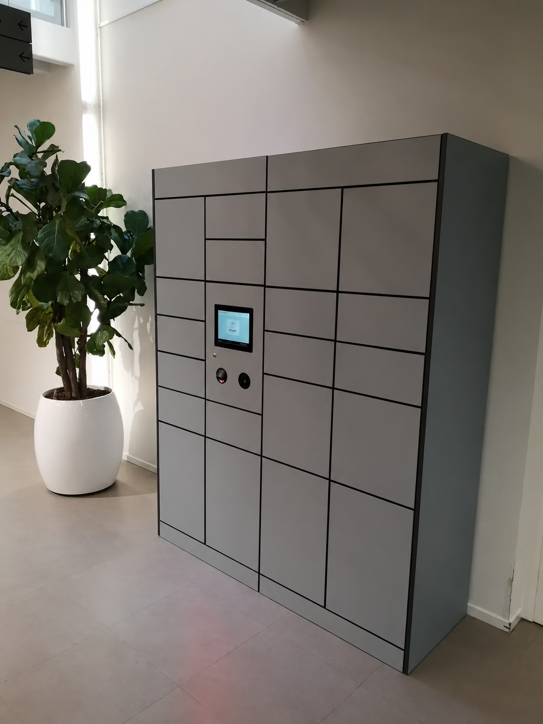 Grey Hublok parcel lockers with an integrated touchscreen beside a potted tree